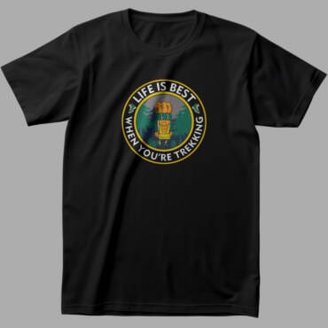Black trekking-themed t-shirt featuring a circular adventure graphic with a backpacker, trees, and mountains, along with the phrase "Life is Best When You're Trekking".