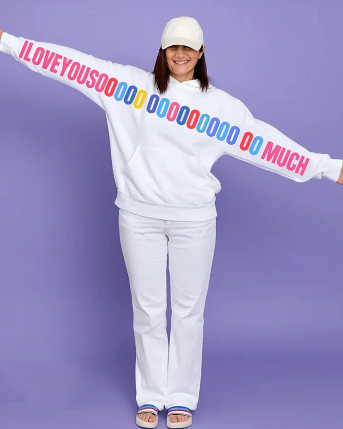 Woman wearing a white unisex hoodie with a colorful “I LOVE YOU SOOOOO MUCH” graphic printed across the sleeves and chest, standing with arms wide open.